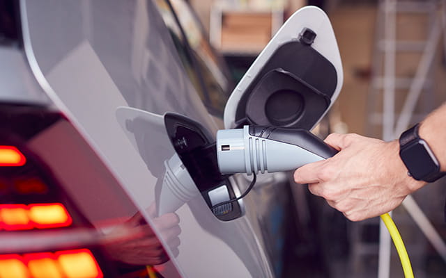 Person schließt ein Elektroauto an einen Ladepunkt an Person schließt ein Elektroauto an einen Ladepunkt an