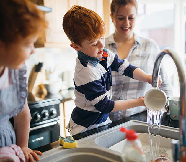 Kleiner Junge wäscht in der Spüle das Geschirr