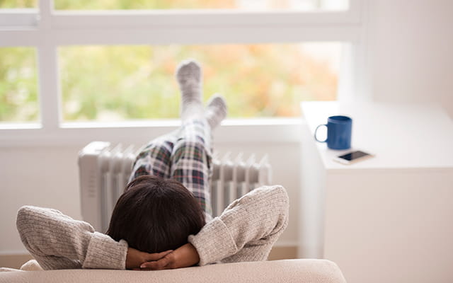 Dame liegt auf einem Sofa mit den Füßen auf der Heizung abgelegt Dame liegt auf einem Sofa mit den Füßen auf der Heizung abgelegt