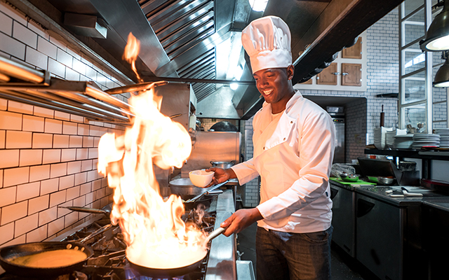 Junger Koch flambiert Essen in einem Restaurant Junger Koch flambiert Essen in einem Restaurant