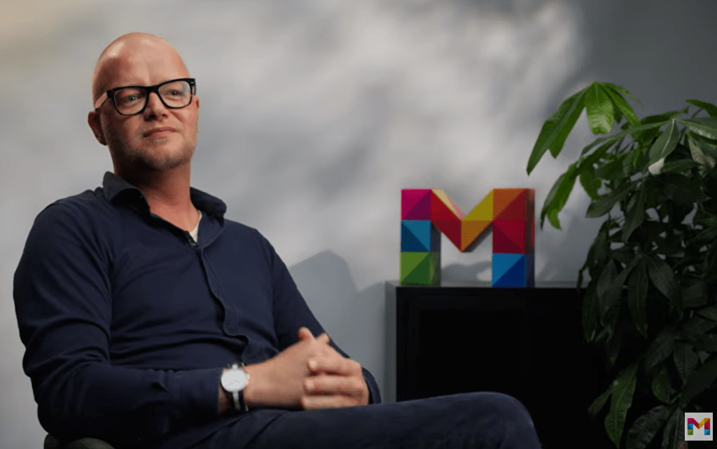 männlicher Mitarbeitender der Mainzer Stadtwerke mit bunten M im Hintergrund