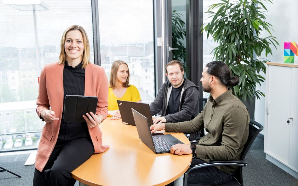 Personen am Meetingtisch mit Tablets und Laptops