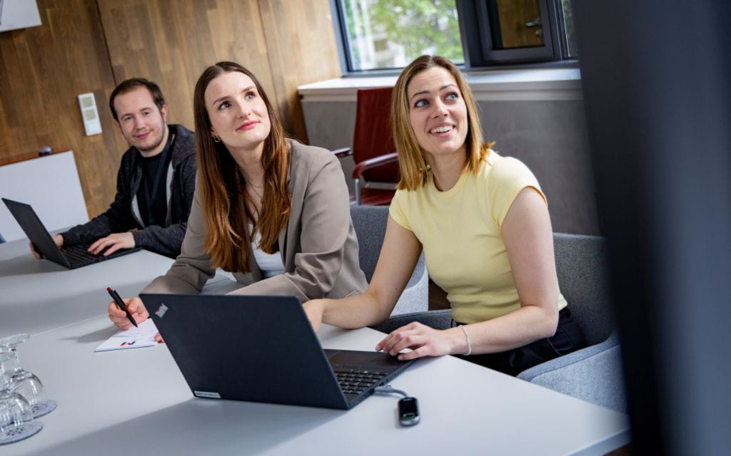 zwei Frauen und ein Mann am Schreibtisch mit Laptop