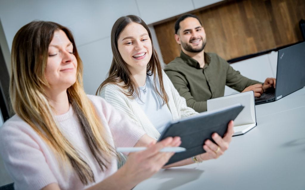 Zwei junge Frauen mit Tablet und ein Mann am Laptop