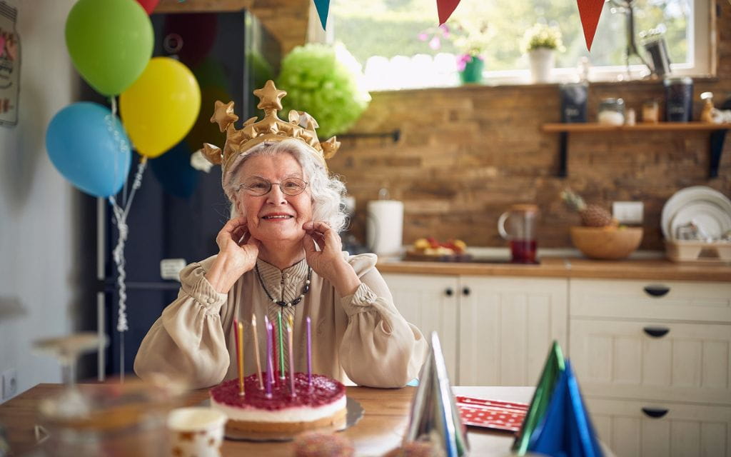 Eine alte Dame mit Luftballons, Geburtstagskuchen und Krone