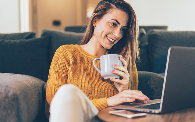 Dame sitzt vor dem Sofa auf dem Boden und arbeitet an einem Laptop Dame sitzt vor dem Sofa auf dem Boden und arbeitet an einem Laptop